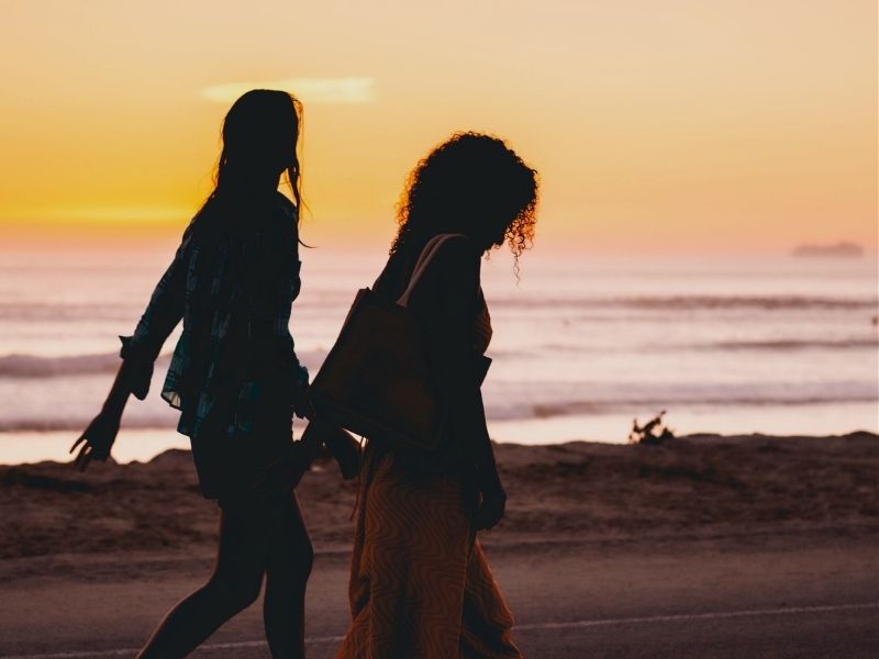 friends walking along beach at sunset
